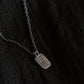 Black fabric background with a blackened silver necklace. The necklace has a fine chain with an octagon shaped pendant with textured surface.