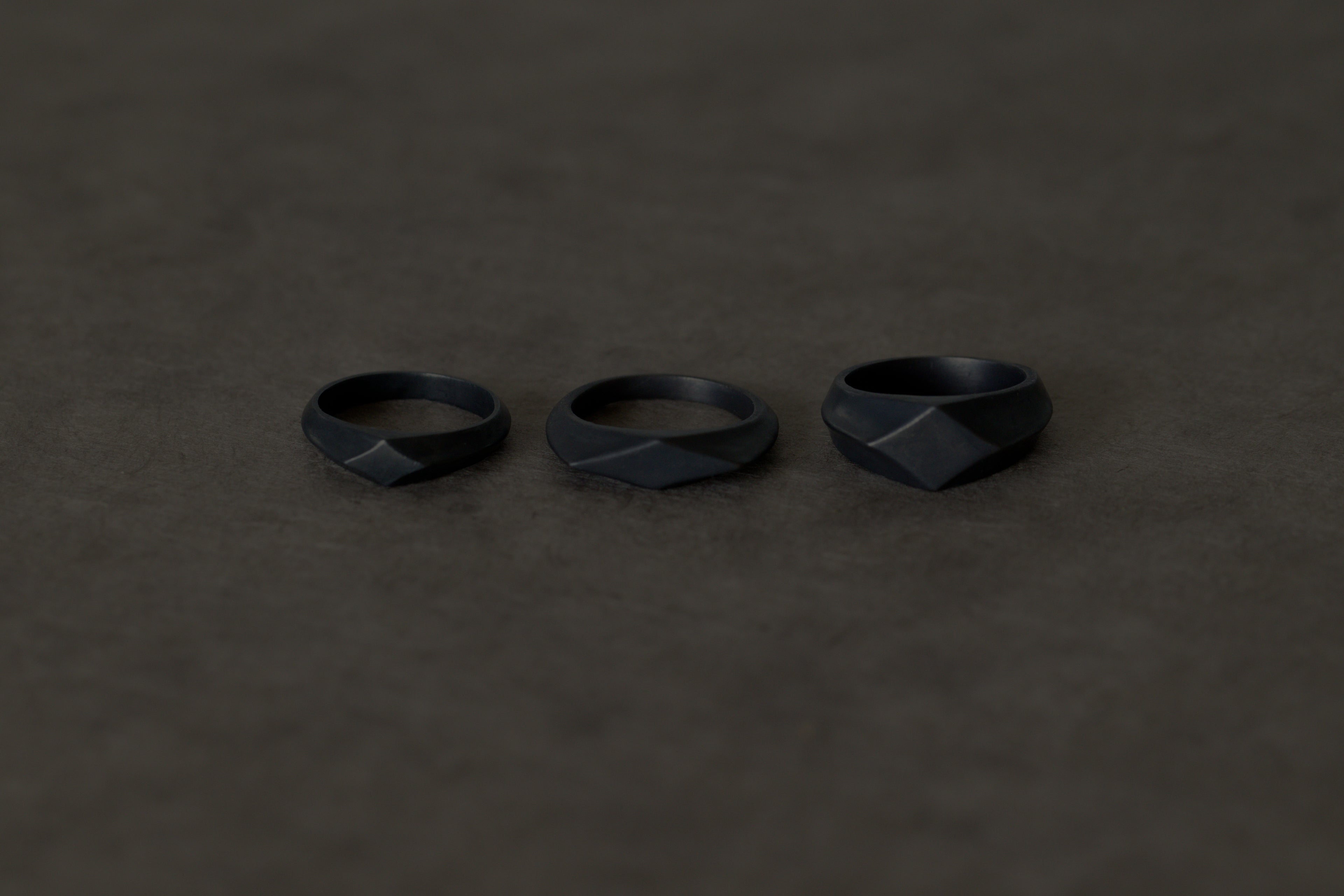 Three matte black rings displayed in a row on a dark beige-brown textured surface.