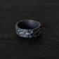 A blackened silver ring with an organic, textured, thorn inspired pattern, resting on a dark, textured surface.