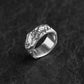 A silver ring with an organic, textured, tree-bark-like pattern, resting on a dark textured surface.