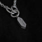 A close up of the silver necklace and the pendant sit on a black fabric background. The image shows parts of the necklace's chain, with three larger rings that connect the geometric pendant. The penant features engravings of a plant and some leaves on the side.